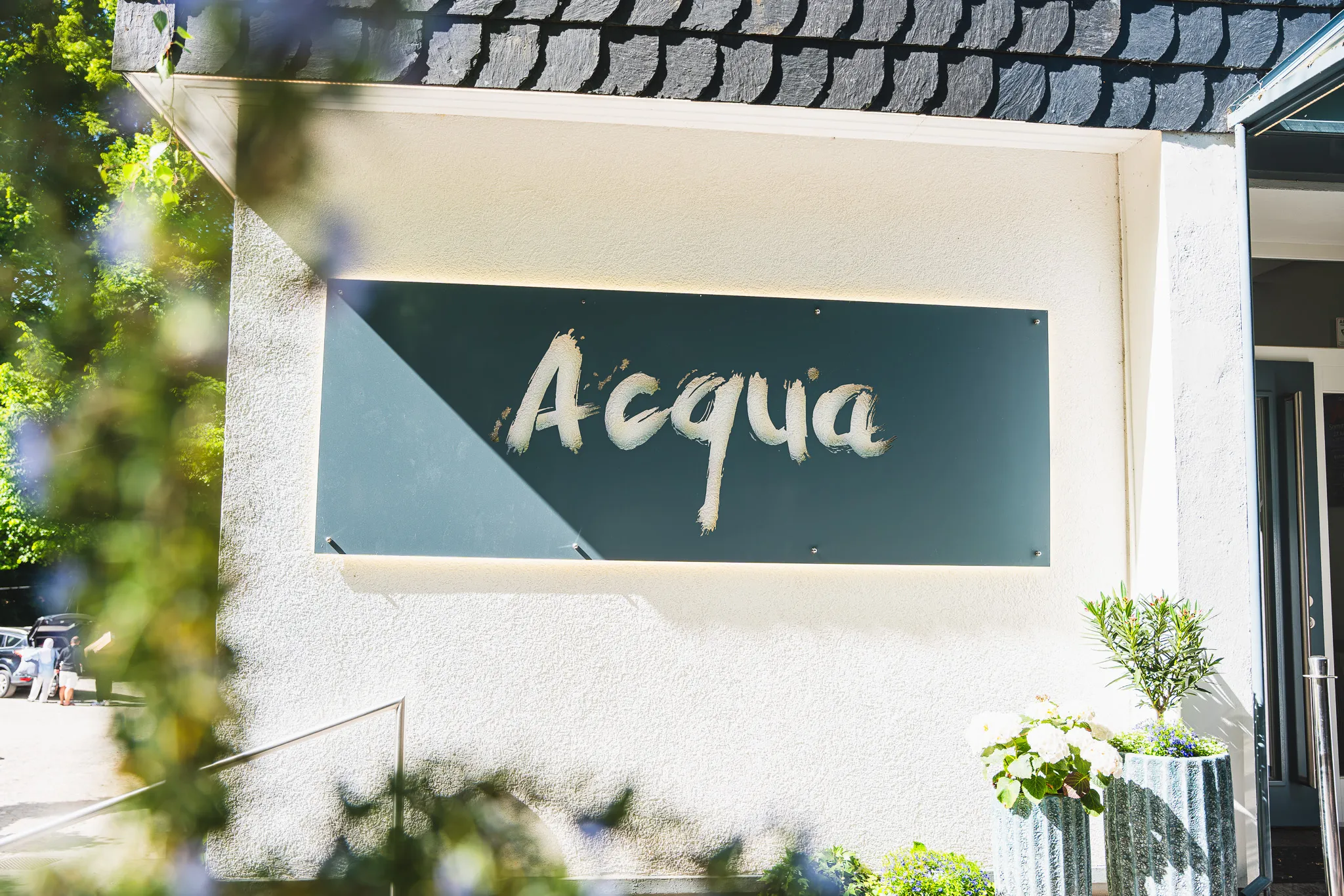 Der Acqua-Schriftzug auf einer dunkelgrünen Tafel an der hellen Fassade.