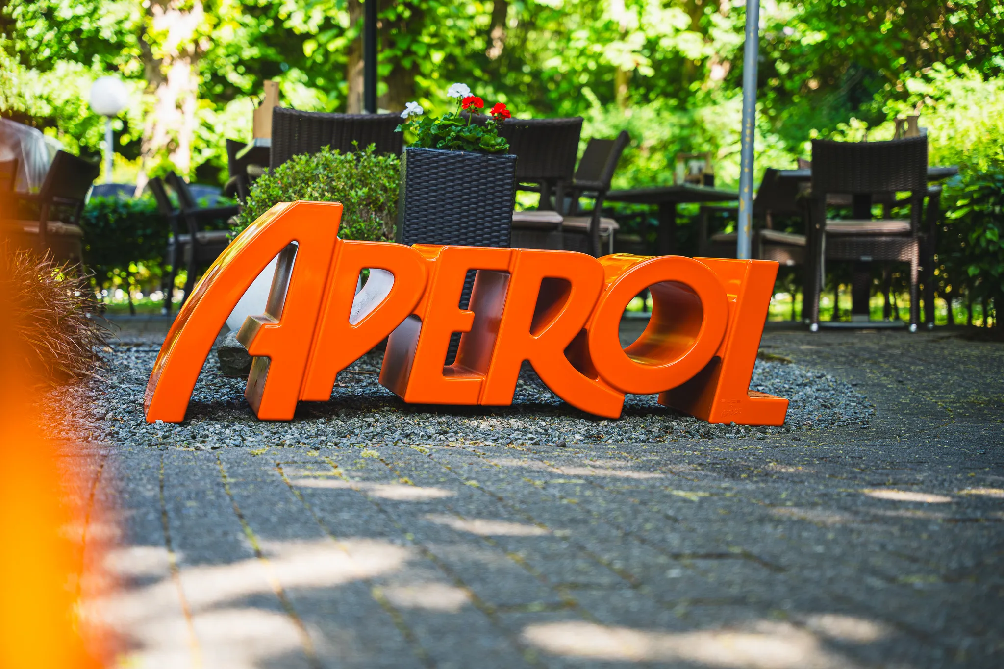 Oranger Aperol-Schriftzug als Aufsteller im Garten des Restaurants.