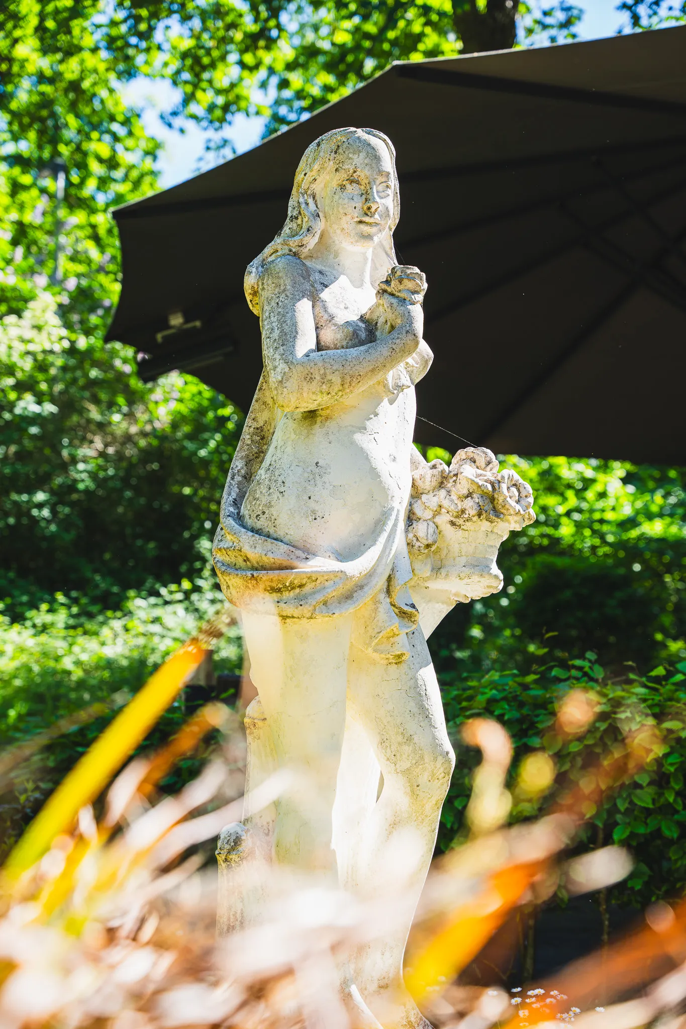 Detailaufnahme der steinernen Gartenfigur vor einem Sonnenschirm.