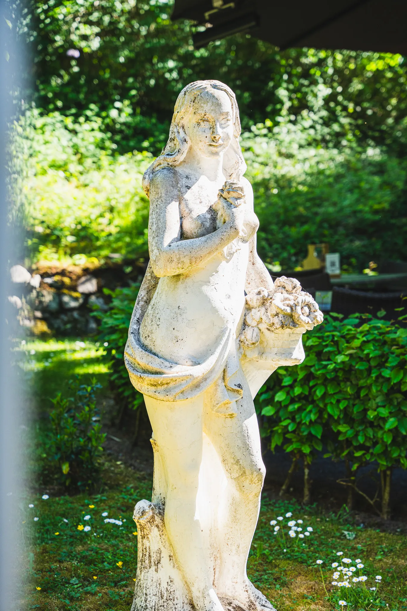 Steinerne Gartenfigur zwischen Grünpflanzen.