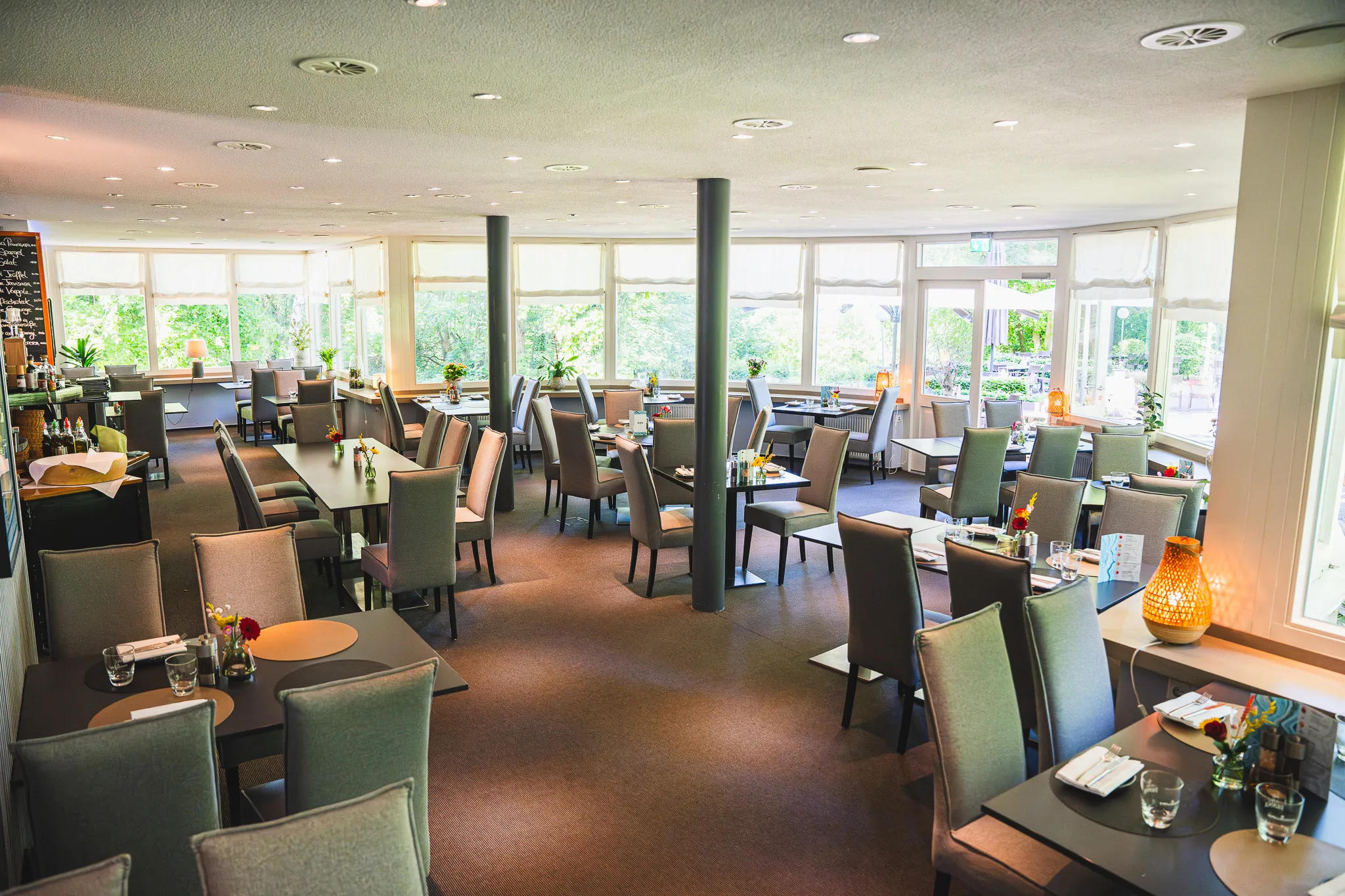 Übersicht des Gastraums mit eingedeckten Tischen und Bar im Hintergrund.