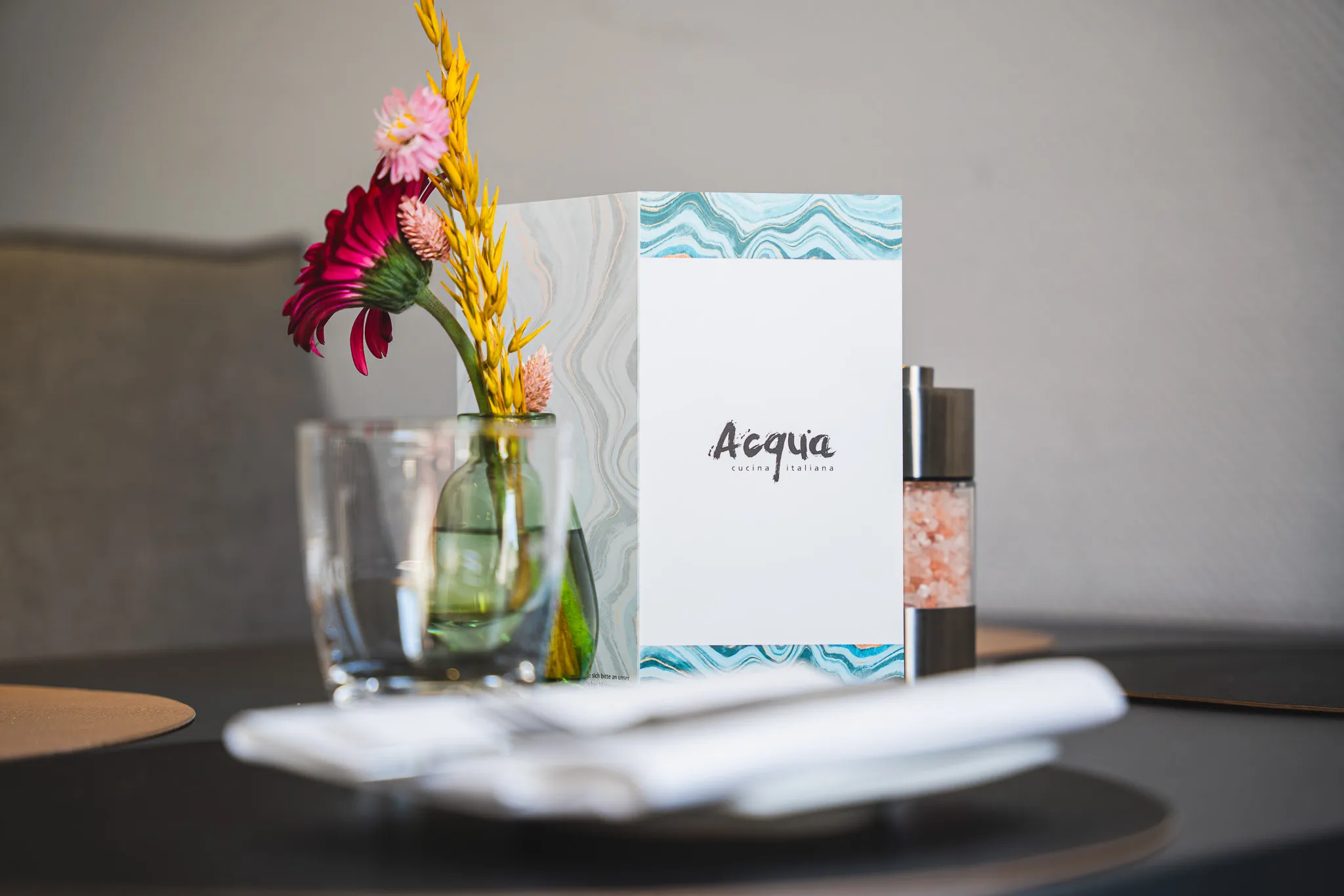 Die Acqua-Menükarte steht auf einem gedeckten Tisch neben einer Vase mit Gerbera.