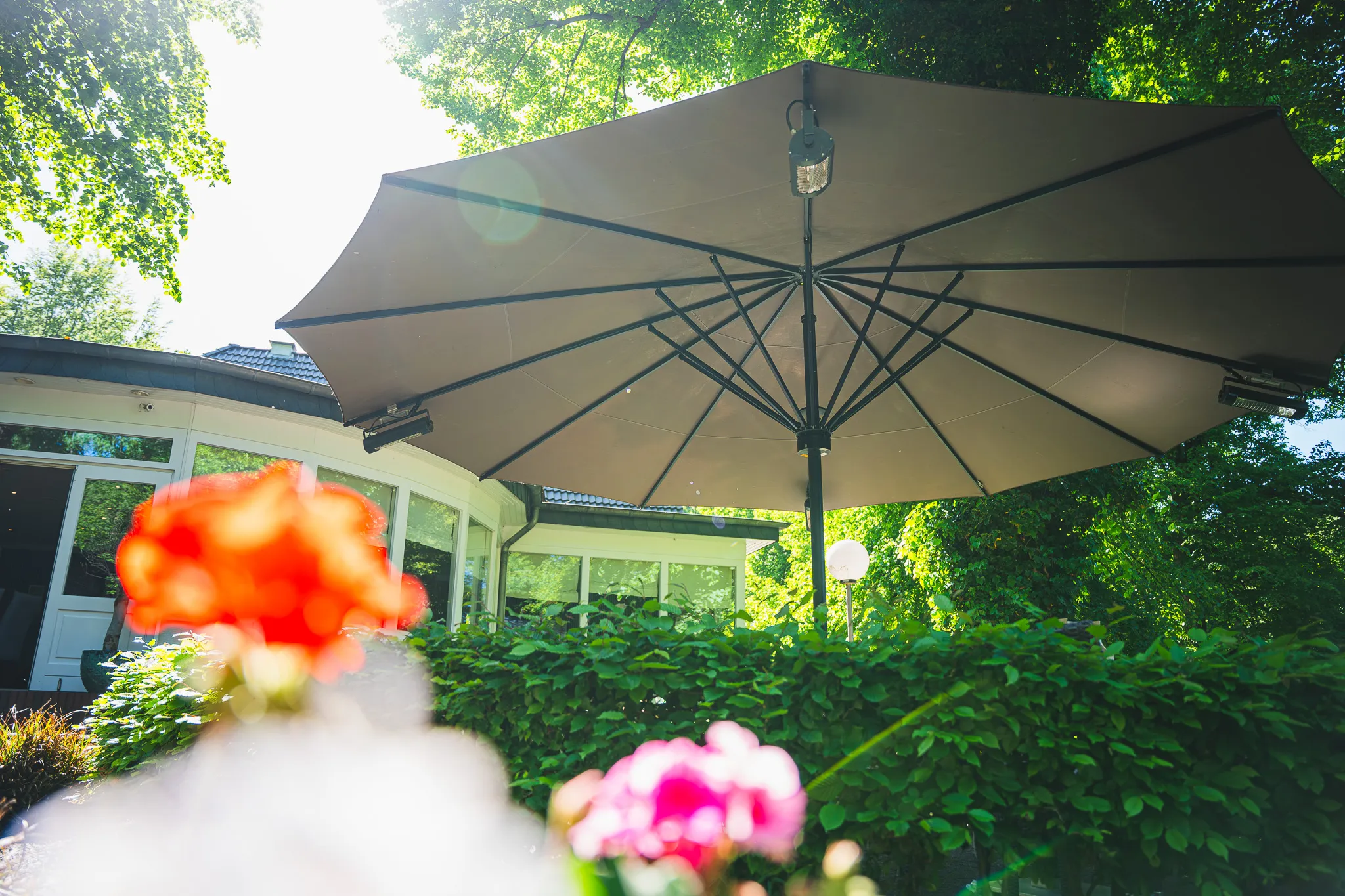 Großer Sonnenschirm über der Terrasse, im Vordergrund rote Blüten.