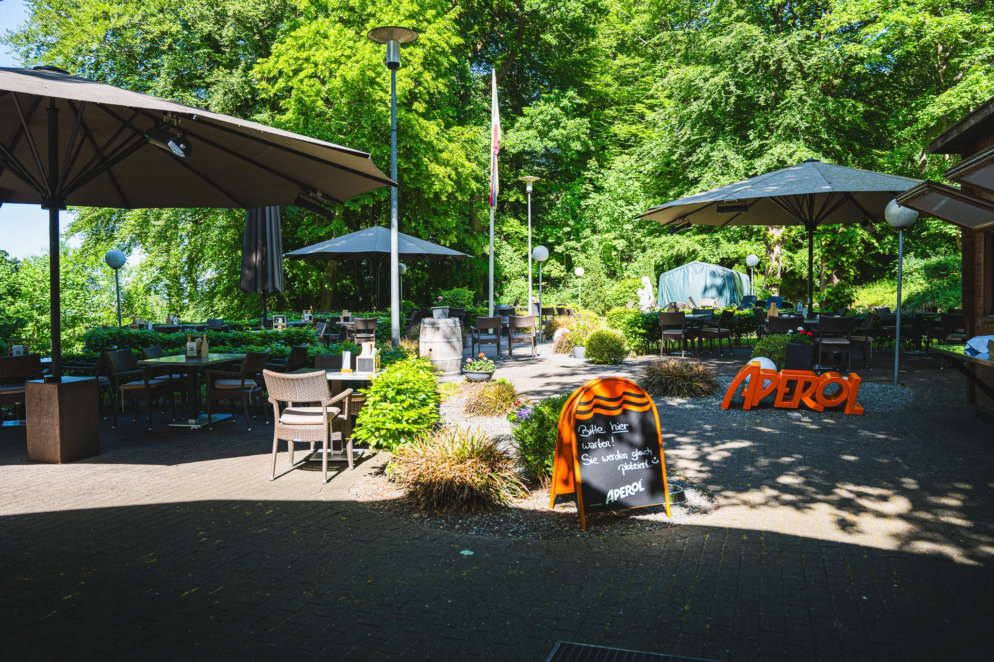 Übersicht der Terrasse mit mehreren Sonnenschirmen und Sitzgruppen im Garten.